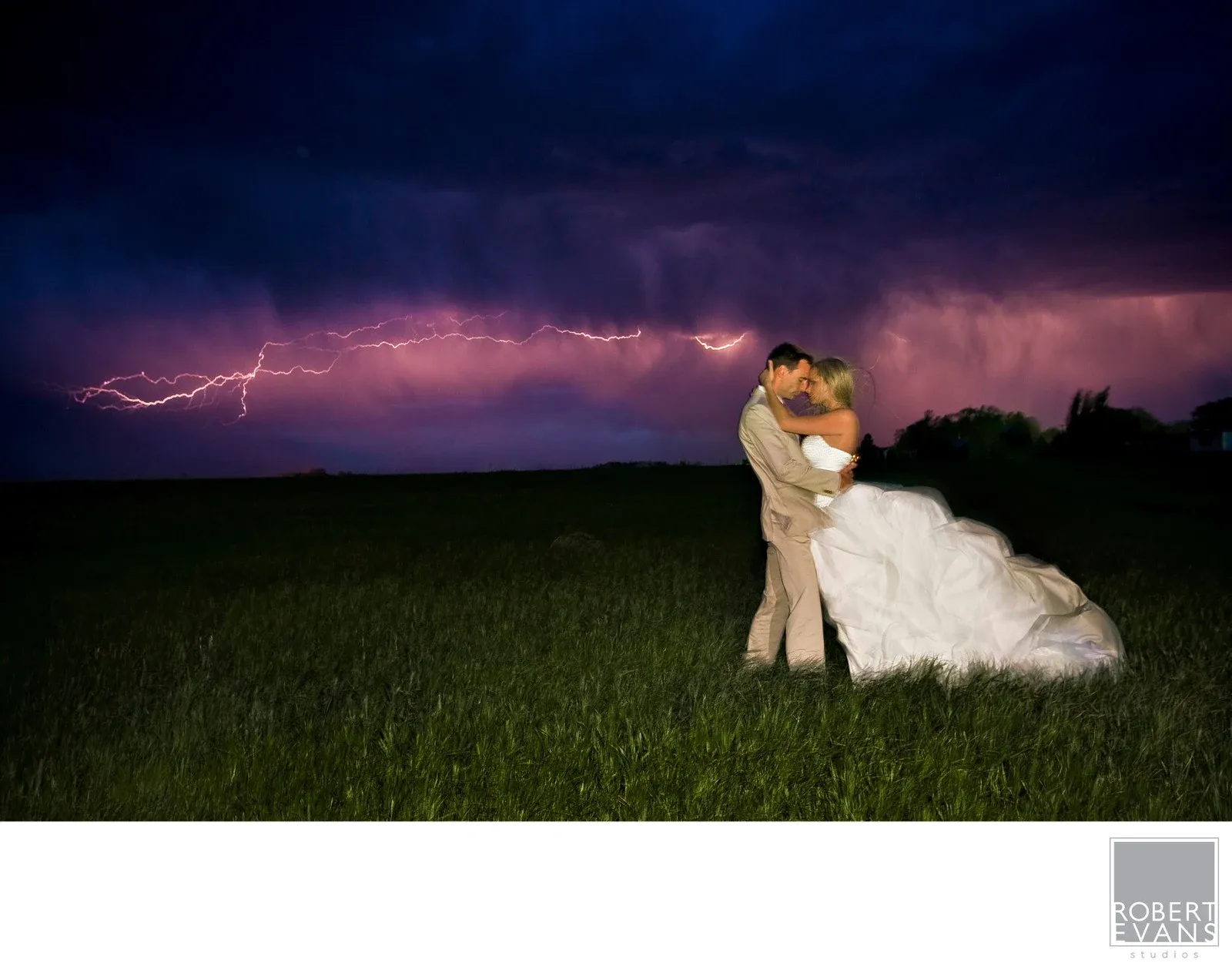 Bride & Groom Kiss as a bolt of lightning flashes in the sky. Newlyweds kissing beneath a purple sky streaked with lightning