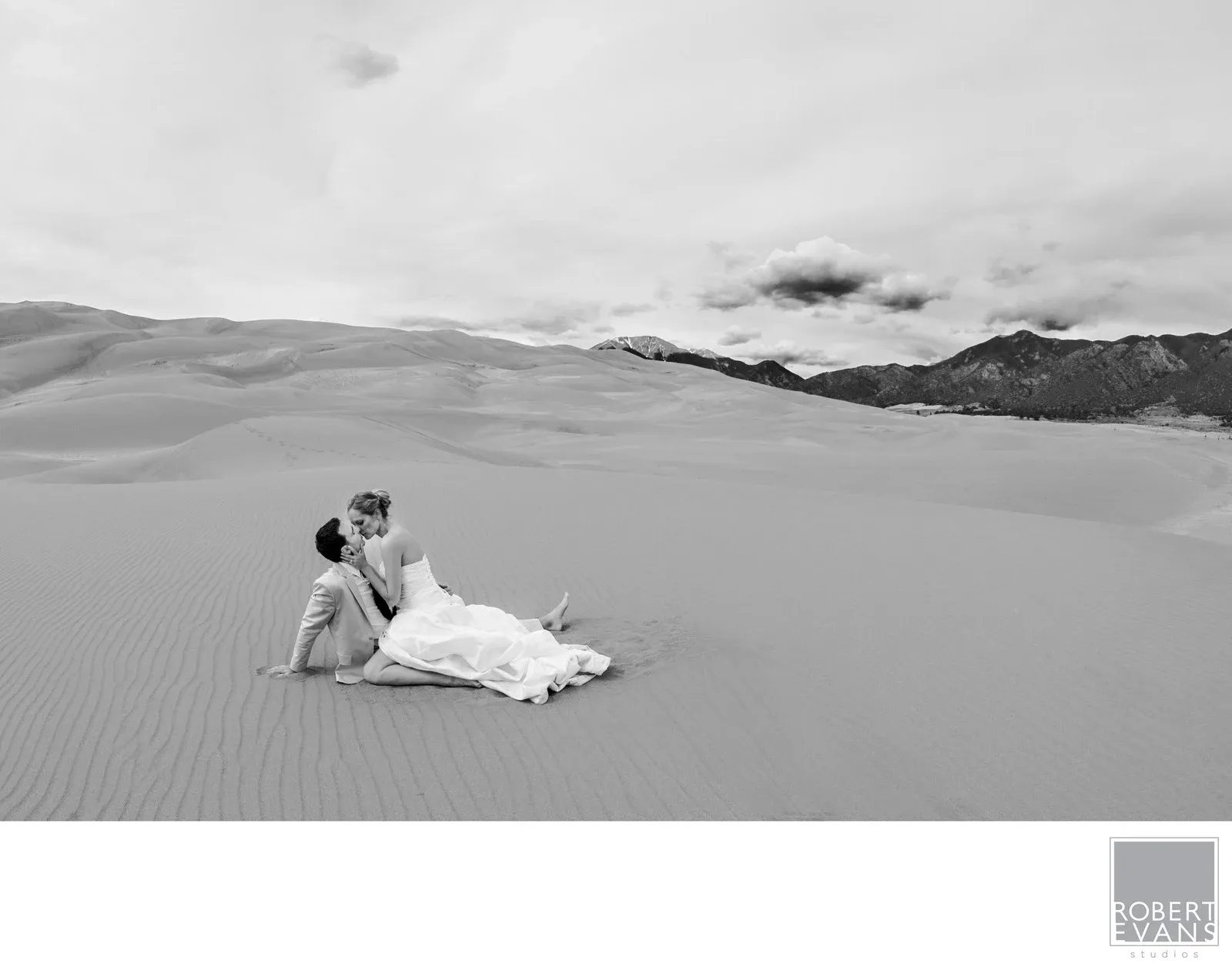 Dune Swoon A bride seated against a wide landscape of sand dunes