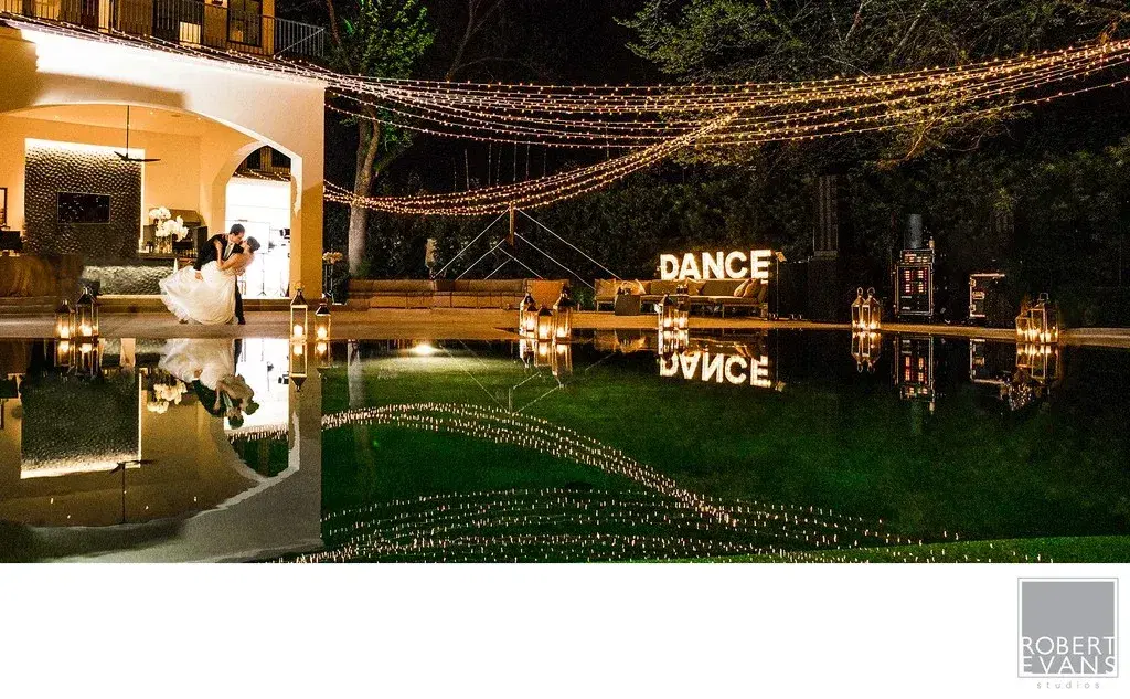 Newlyweds reflected in a pool beneath reception string lights Newlyweds reflected in a pool beneath reception string lights